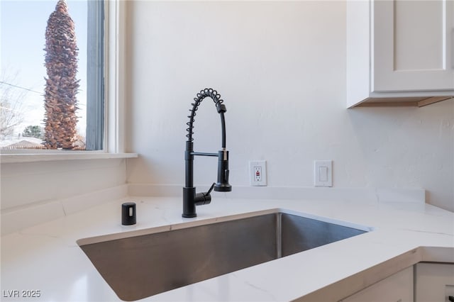 interior details with white cabinets, light stone countertops, and a sink
