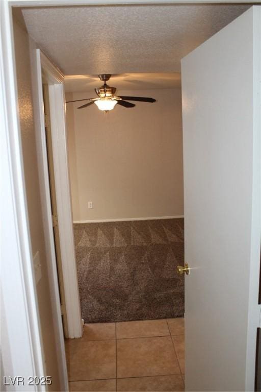 hallway with light carpet, a textured ceiling, and light tile patterned flooring