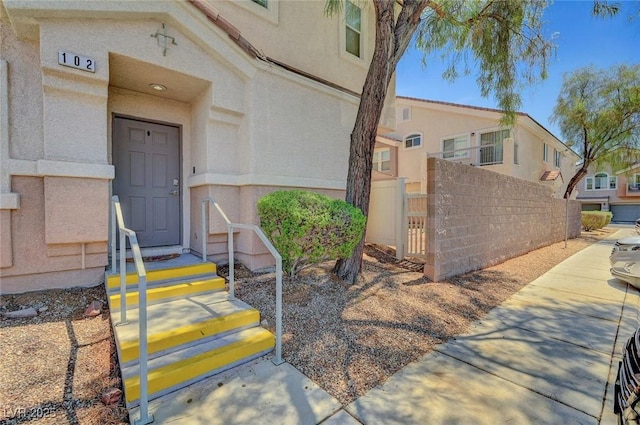 doorway to property featuring fence and stucco siding