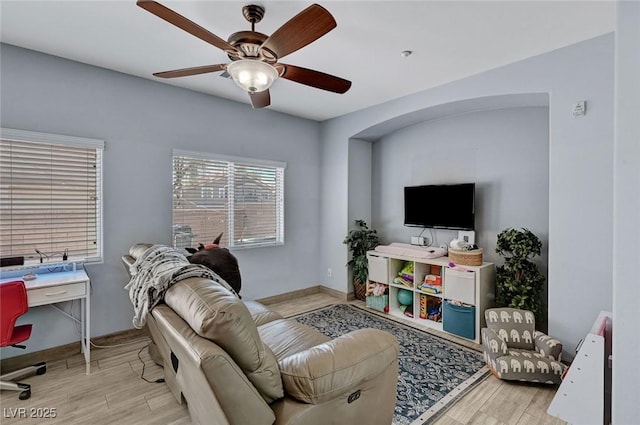 living area featuring wood finished floors, ceiling fan, a desk, and baseboards