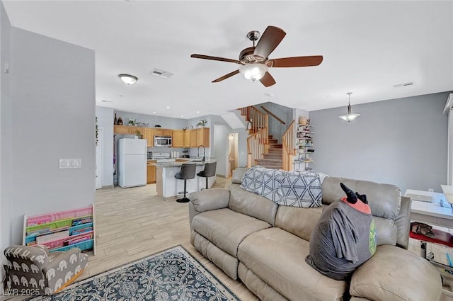 living area with stairway, light wood-style flooring, a ceiling fan, and baseboards