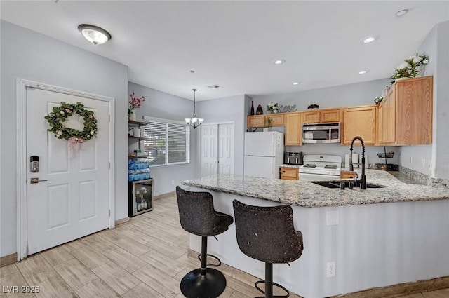 kitchen featuring white appliances, a sink, a peninsula, light stone countertops, and a chandelier