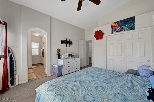 carpeted bedroom with arched walkways, vaulted ceiling, a ceiling fan, a closet, and connected bathroom