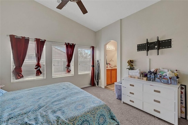 bedroom featuring lofted ceiling, arched walkways, light carpet, a ceiling fan, and ensuite bath