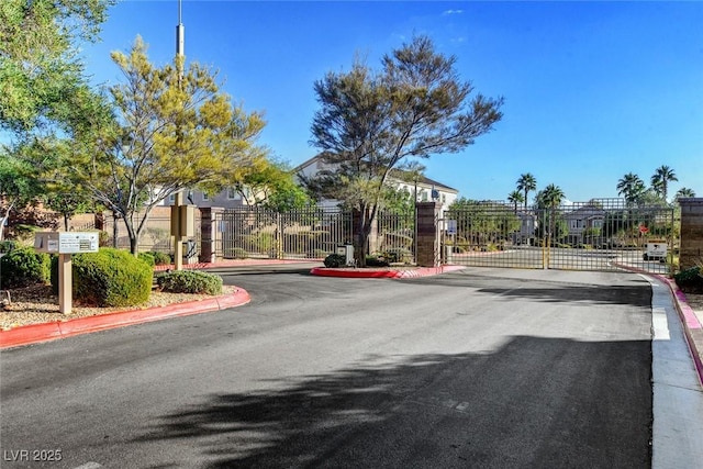 view of asphalt street with a gate, curbs, and a gated entry