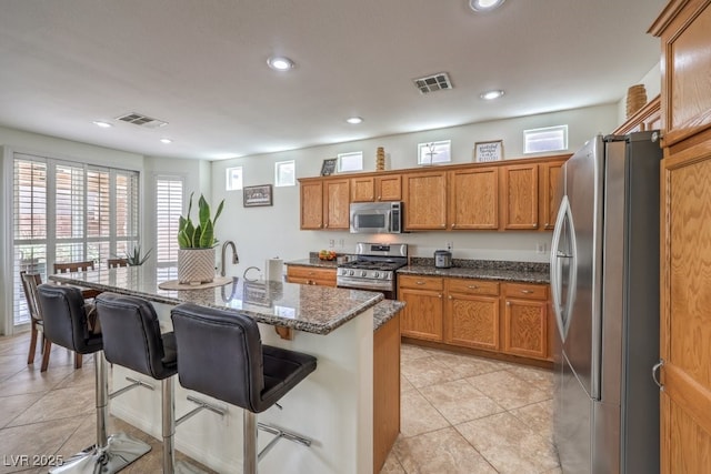 10294 Running Falls St, Las Vegas, NV 89178 - kitchen featuring stainless steel appliances, brown cabinets, a breakfast bar area, dark stone counters, and recessed lighting