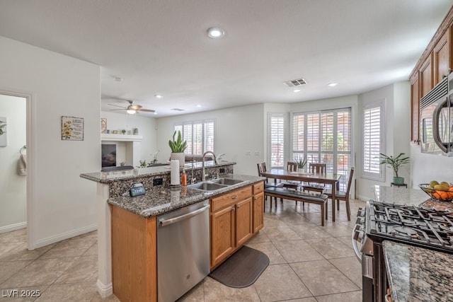 10294 Running Falls St, Las Vegas, NV 89178 - kitchen with appliances with stainless steel finishes, a sink, a center island with sink, brown cabinetry, and dark stone counters