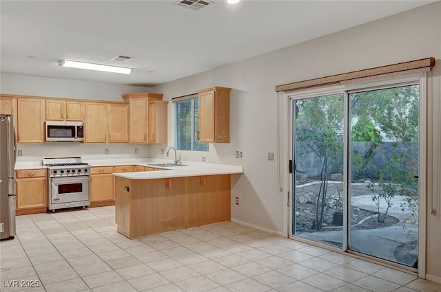 kitchen with appliances with stainless steel finishes, a sink, light brown cabinets, a peninsula, and light countertops