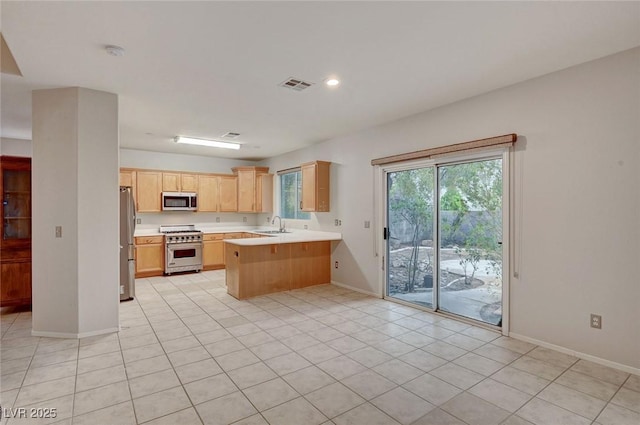 kitchen featuring stainless steel appliances, light brown cabinetry, a peninsula, light countertops, and a sink