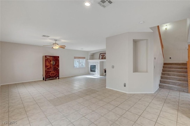 unfurnished living room with ceiling fan, stairs, a fireplace, light tile patterned floors, and baseboards