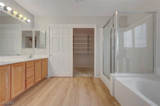 bathroom featuring wood finished floors, a shower stall, double vanity, and a bath
