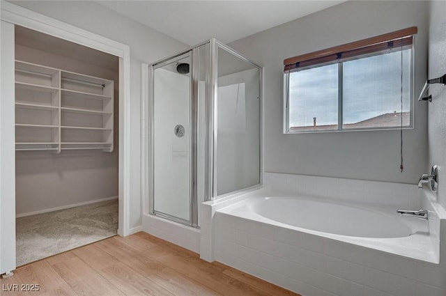 bathroom with a shower stall, wood finished floors, a bath, and a spacious closet