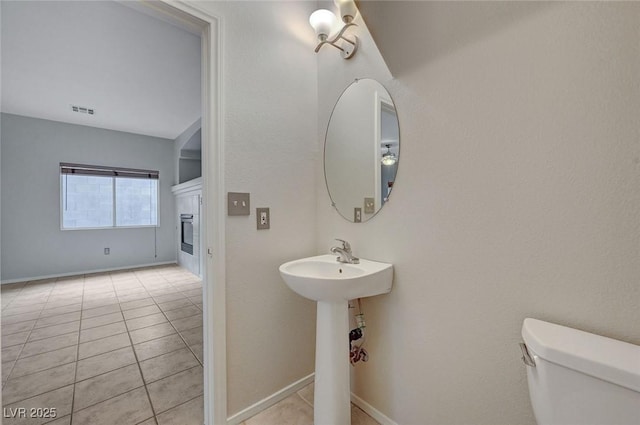 bathroom featuring a tile fireplace, toilet, tile patterned flooring, and baseboards