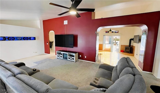 carpeted living room with ceiling fan, a wood stove, lofted ceiling, and arched walkways