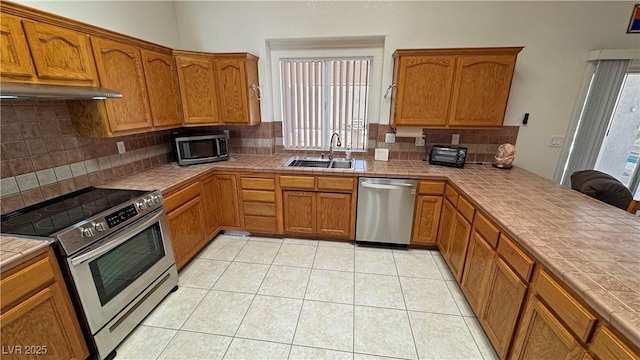 kitchen featuring a sink, tasteful backsplash, under cabinet range hood, tile counters, and appliances with stainless steel finishes