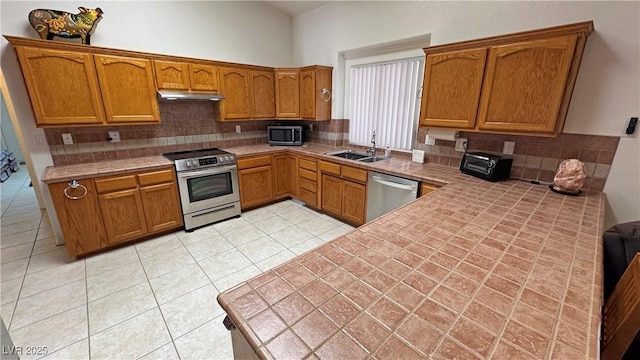 kitchen featuring brown cabinets, decorative backsplash, appliances with stainless steel finishes, and a sink