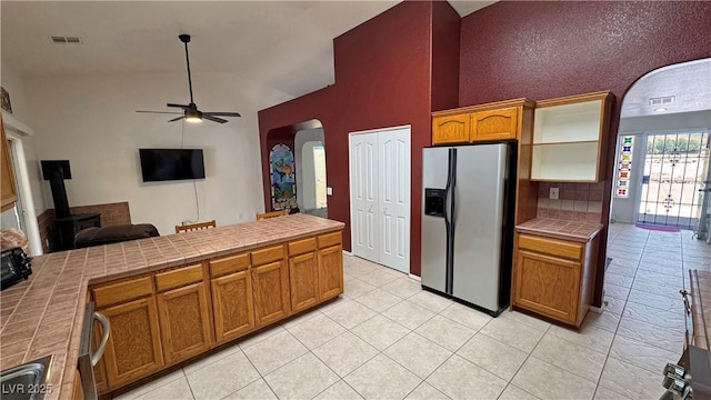 kitchen featuring a wood stove, stainless steel fridge with ice dispenser, tile counters, and arched walkways