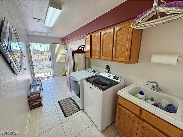 laundry area with washer and clothes dryer, a sink, cabinet space, a textured ceiling, and light tile patterned flooring