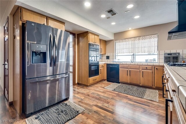 5242 Dickens Dr, Las Vegas, NV 89119 - kitchen featuring wall chimney range hood, tasteful backsplash, black appliances, visible vents, and tile counters