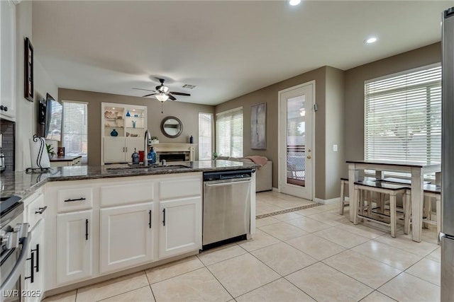 kitchen featuring a sink, stainless steel appliances, dark stone counters, a fireplace, and a ceiling fan