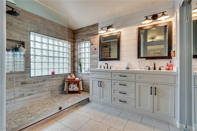 bathroom featuring lofted ceiling, a sink, tile patterned flooring, tiled shower, and double vanity