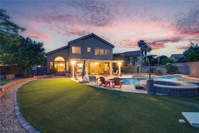 back of property with a lawn, a patio area, an in ground hot tub, and a fenced backyard