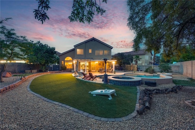 back of property at dusk featuring a patio area, a pool with connected hot tub, a lawn, and a fenced backyard