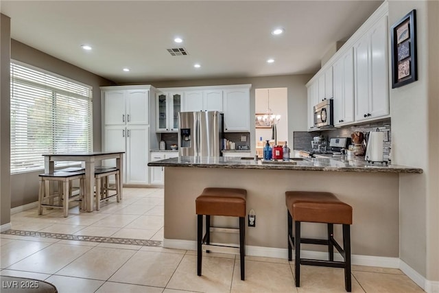 kitchen featuring visible vents, white cabinetry, a peninsula, decorative backsplash, and stainless steel appliances
