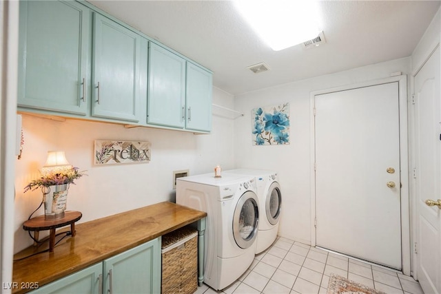 laundry area featuring washing machine and clothes dryer, light tile patterned floors, visible vents, and cabinet space