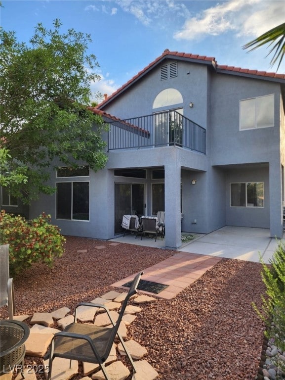 back of house with a tiled roof, a patio area, stucco siding, and a balcony