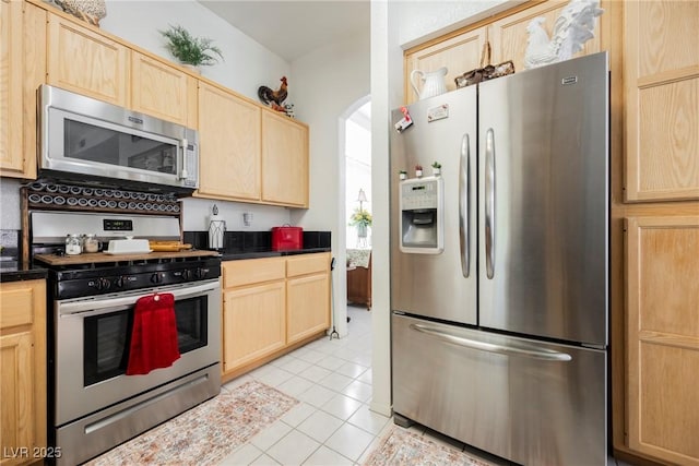 kitchen featuring dark countertops, stainless steel appliances, light tile patterned flooring, and light brown cabinetry