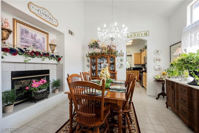 dining room featuring a notable chandelier, a tiled fireplace, visible vents, high vaulted ceiling, and arched walkways