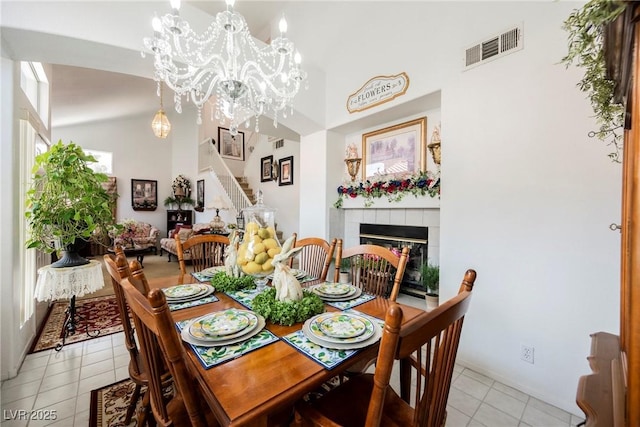 dining area with lofted ceiling, a tile fireplace, visible vents, a chandelier, and stairway