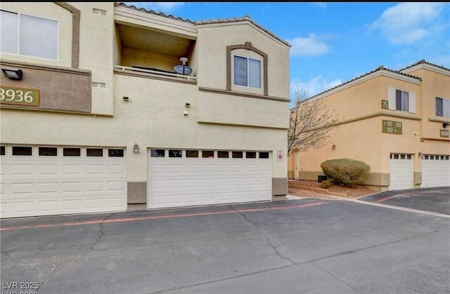 townhome / multi-family property with stucco siding, a garage, and a tile roof