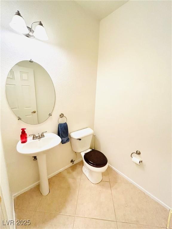 half bath featuring toilet, tile patterned flooring, baseboards, and a sink