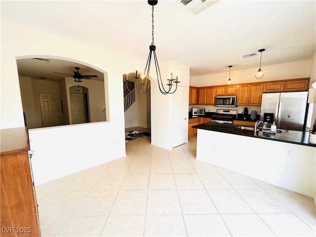 kitchen featuring appliances with stainless steel finishes, dark countertops, arched walkways, brown cabinets, and ceiling fan