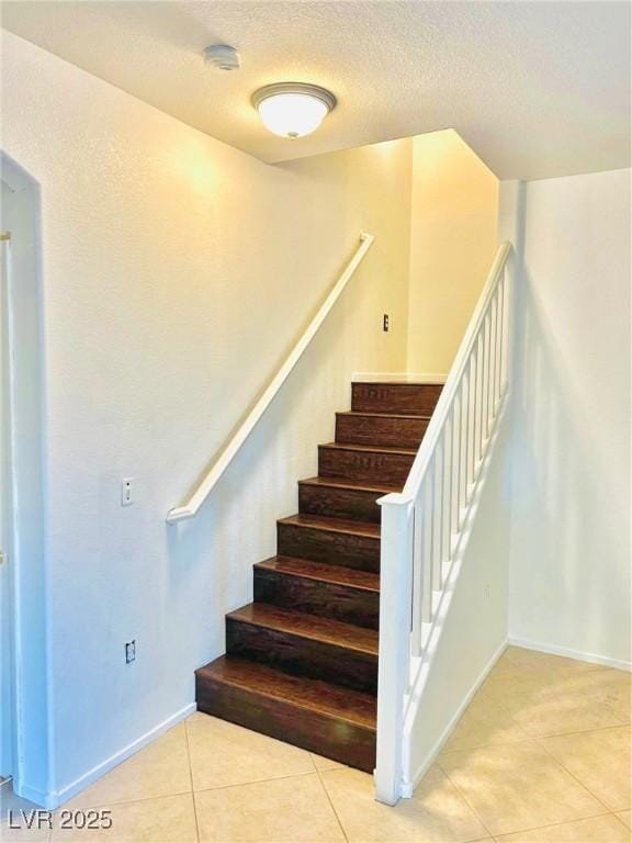 stairs with tile patterned flooring, baseboards, and a textured ceiling
