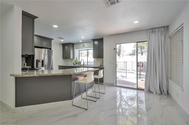 8404 Shore Breeze Dr, Las Vegas, NV 89128 - kitchen featuring stainless steel fridge, a peninsula, light stone countertops, light marble finish floors, and recessed lighting