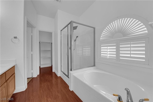 full bathroom featuring wood finished floors, vanity, a shower stall, a walk in closet, and a bath