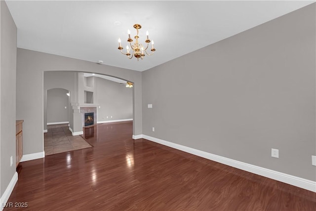 spare room with wood finished floors, a lit fireplace, baseboards, and arched walkways