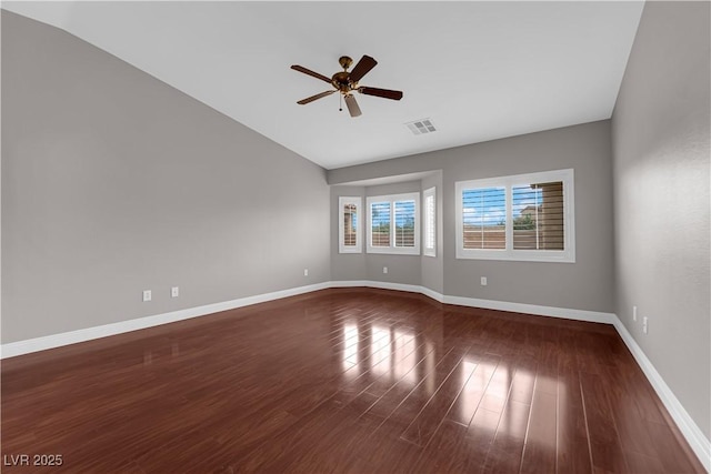 spare room with lofted ceiling, dark wood-type flooring, visible vents, a ceiling fan, and baseboards