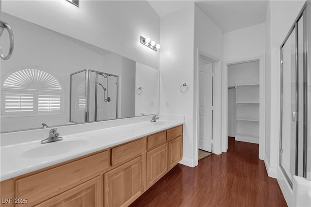 full bath featuring a stall shower, double vanity, a sink, and wood finished floors
