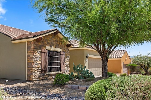 exterior space with stone siding, stucco siding, an attached garage, and a tile roof