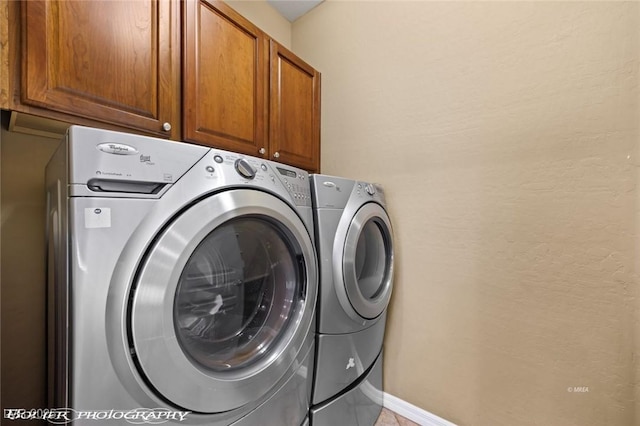 clothes washing area with washing machine and dryer, cabinet space, and baseboards