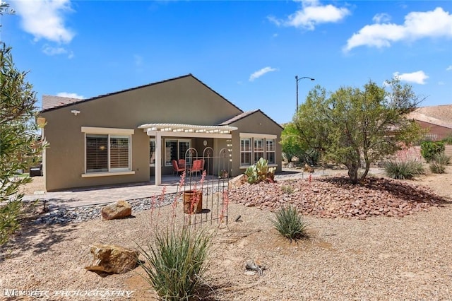 rear view of house featuring stucco siding, a pergola, and a patio area