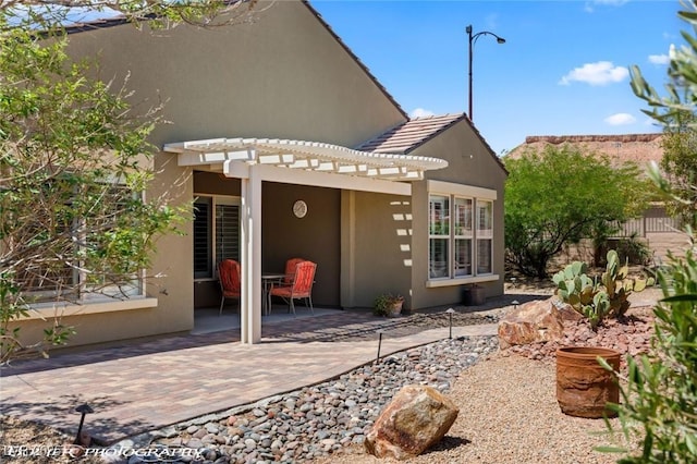 rear view of property with a pergola, a patio area, and stucco siding