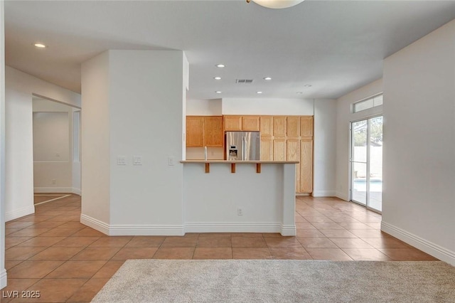 kitchen featuring light tile patterned floors, visible vents, stainless steel fridge with ice dispenser, a kitchen breakfast bar, and a peninsula