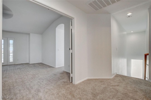 carpeted spare room featuring visible vents, baseboards, lofted ceiling, and arched walkways