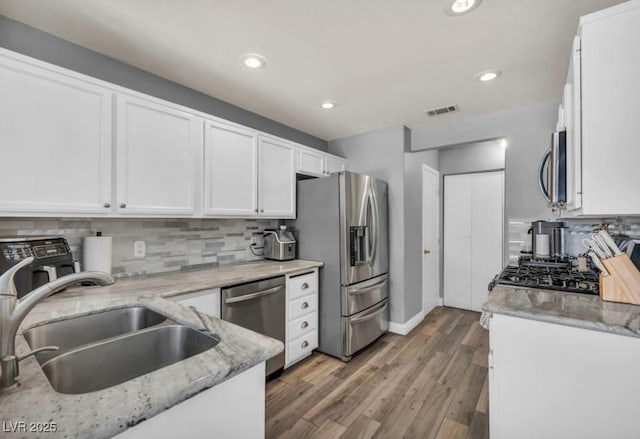 5024 Starfinder Ave, Las Vegas, NV 89108 - kitchen with stainless steel appliances, a sink, white cabinetry, tasteful backsplash, and light wood-style floors