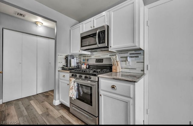 5024 Starfinder Ave, Las Vegas, NV 89108 - kitchen with appliances with stainless steel finishes, light wood-type flooring, white cabinetry, light stone counters, and decorative backsplash